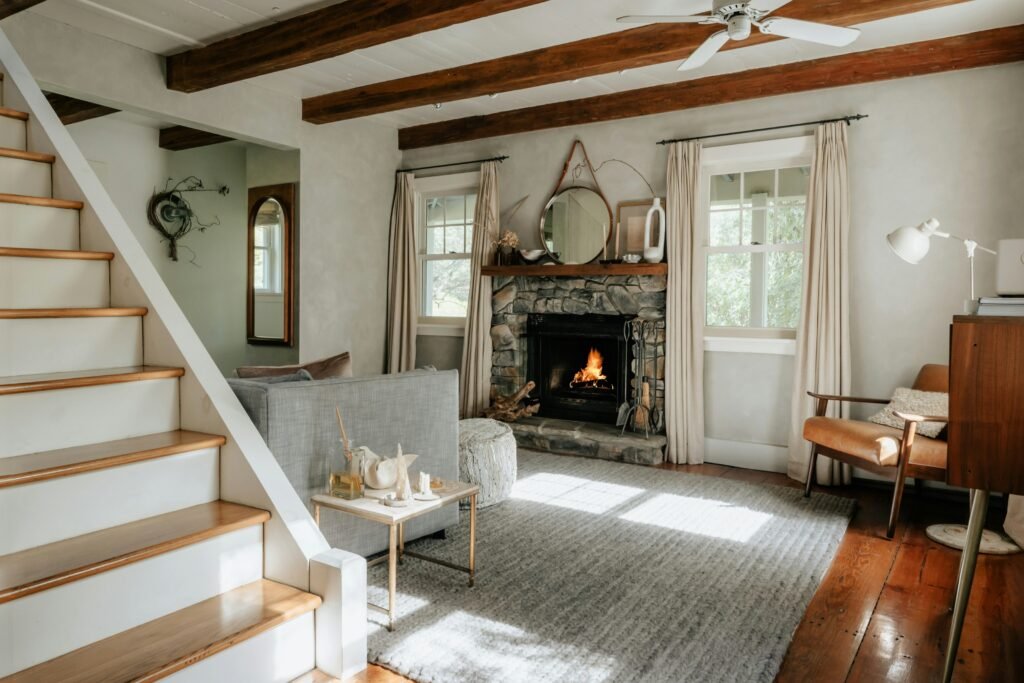 a cozy cottage interior living room with a fireplace going and wooden beams on the ceiling