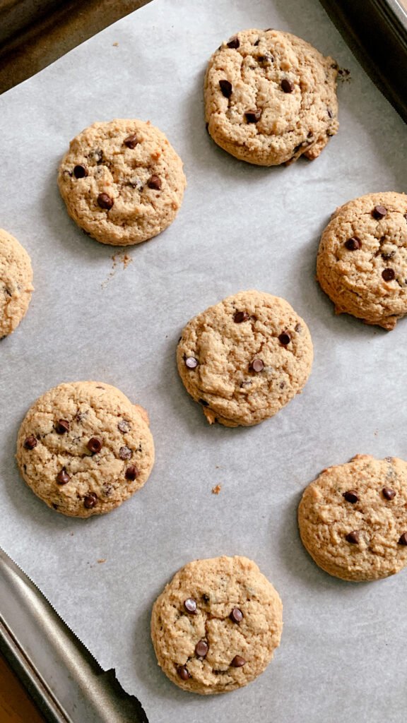 fresh milled chocolate chip cookies on a layer of parchment paper on a cookie sheet