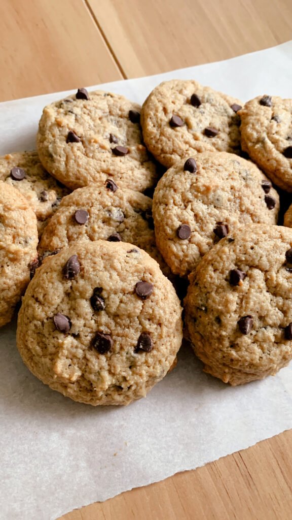 fresh milled chocolate chip cookies on a layer of parchment paper on a wood table