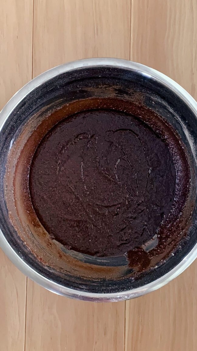 Ingredients mixed together for Texas sheet cake in a stainless steel bowl on a wooden surface