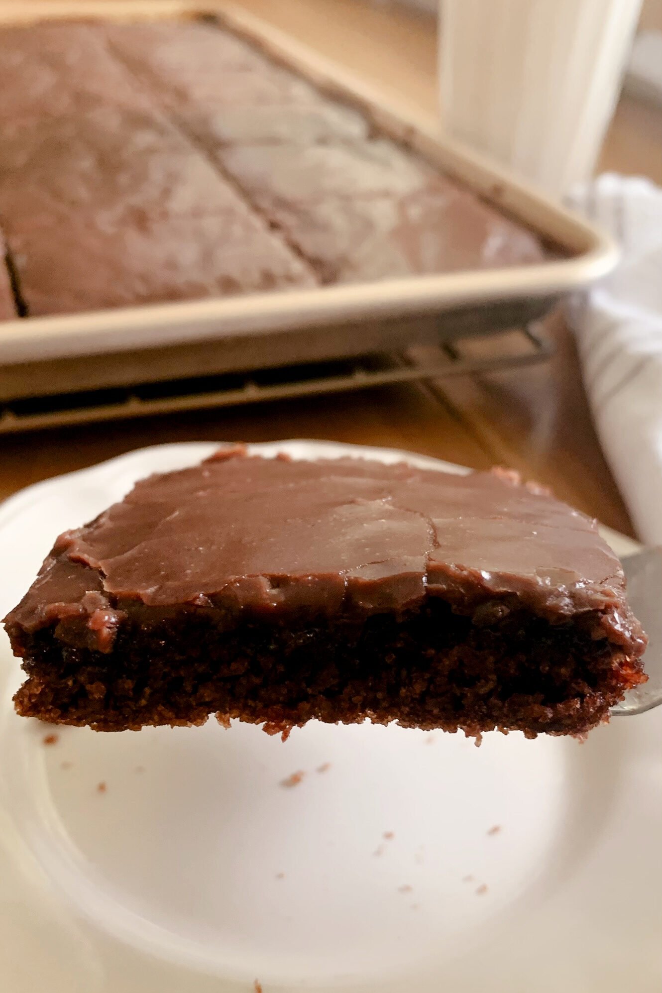 A slice of fresh milled Texas sheet cake lifted on a fork over a white plate.