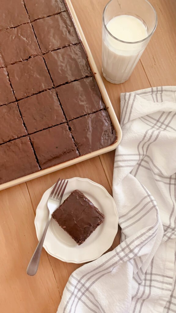 fresh milled Texas sheet cake next to a glass of milk and a tea towel by a slice of fresh milled Texas sheet cake and a fork on a plate