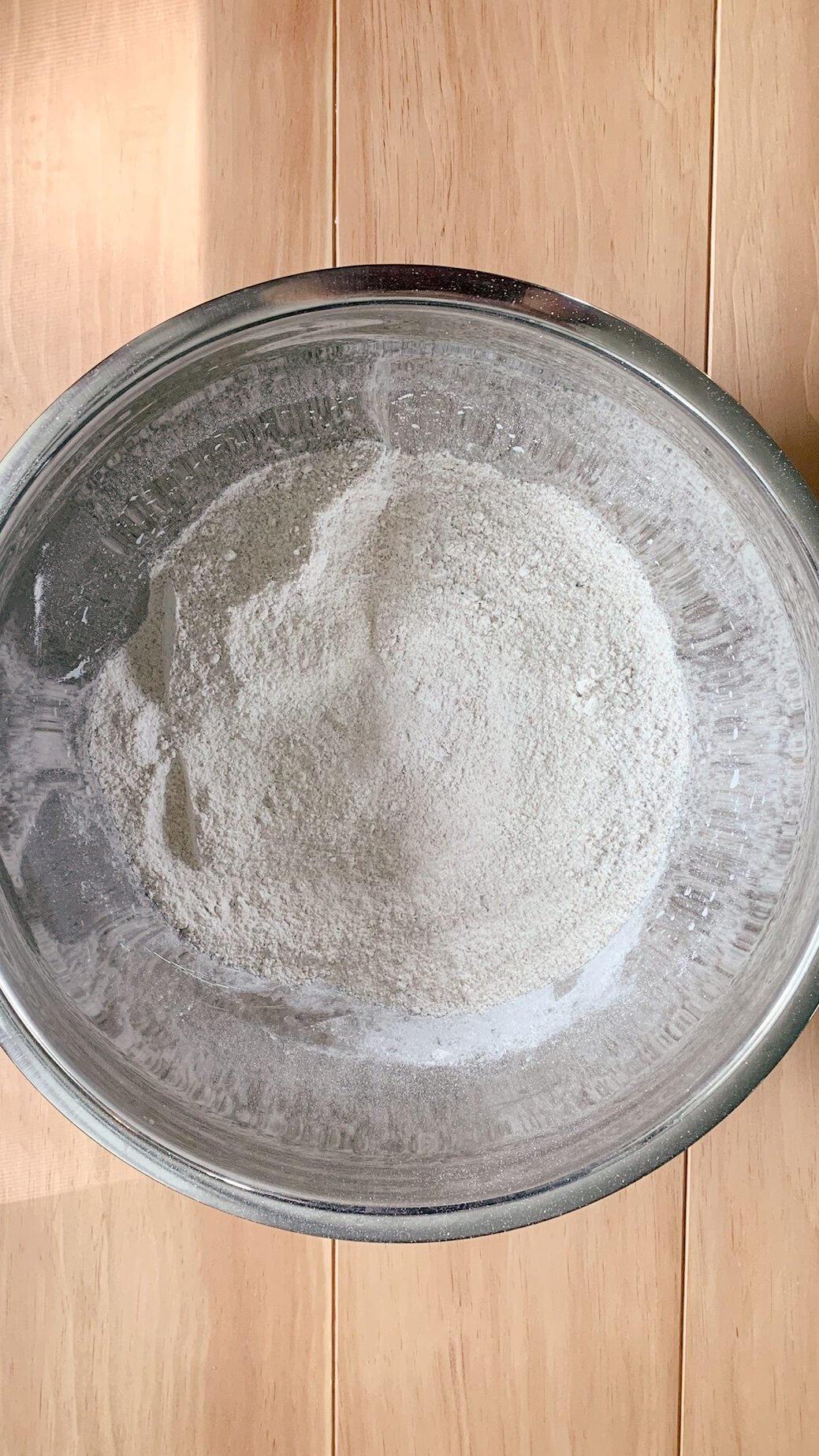 Flour and sugar mixed together, ingredients for fresh milled Texas sheet cake in a stainless steel bowl on a wooden surface
