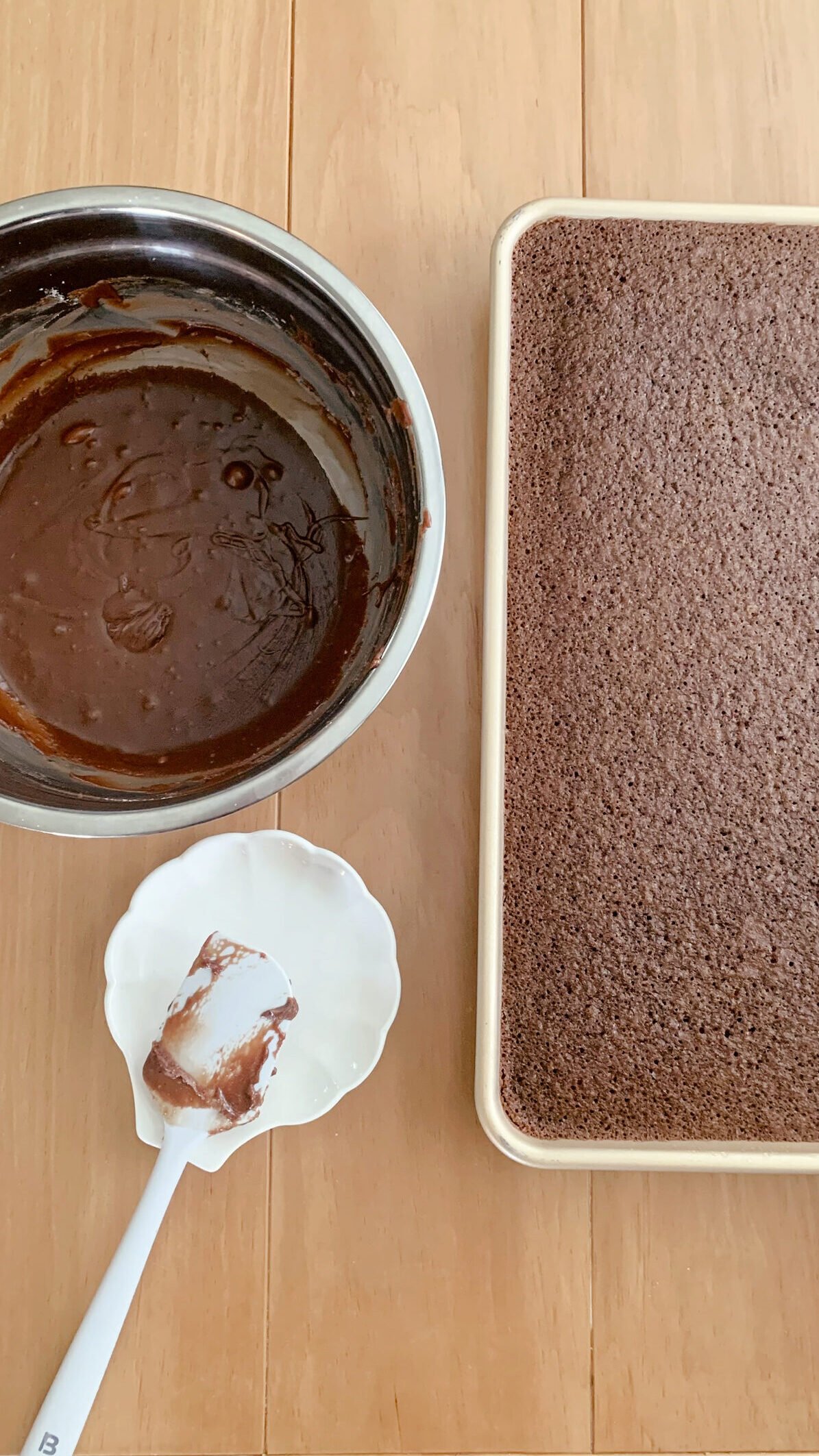 Chocolate icing next to a fresh milled Texas sheet cake with a spatula ready to be iced