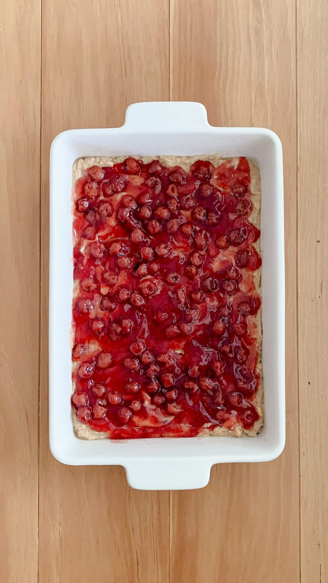 The cherry pie filling layer of fresh milled cherry coffee cake batter spread out evenly over the batter, on a wooden surface
