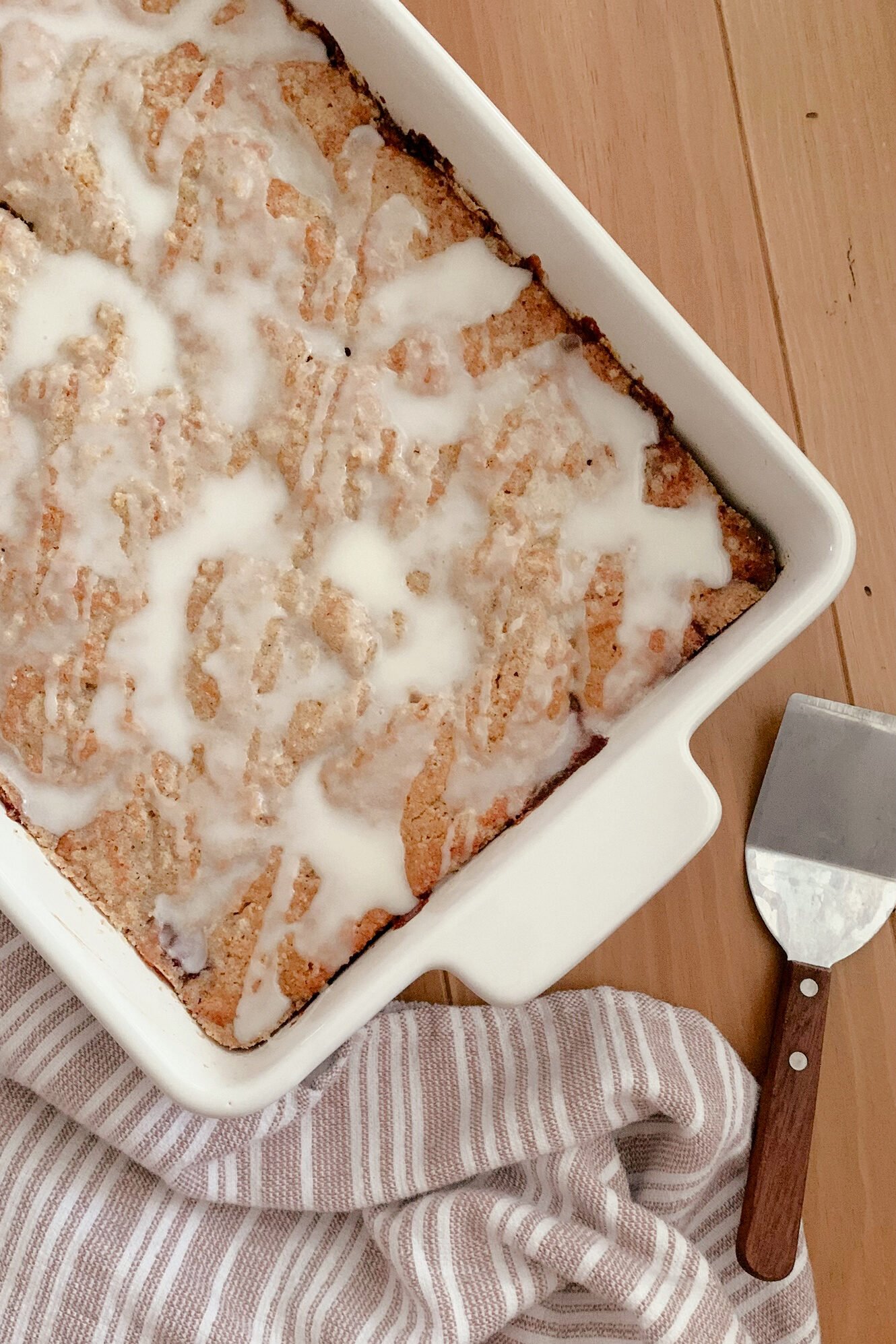 Fresh Milled Cherry Coffee Cake next to a tea towel and serving utensil on a wooden surface.