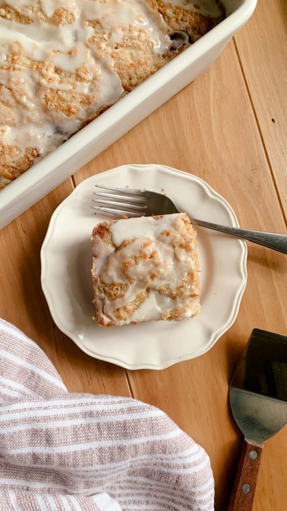 Fresh Milled Cherry Coffee Cake on a plate with a fork next to a tea towel and serving utensil on a wooden surface.