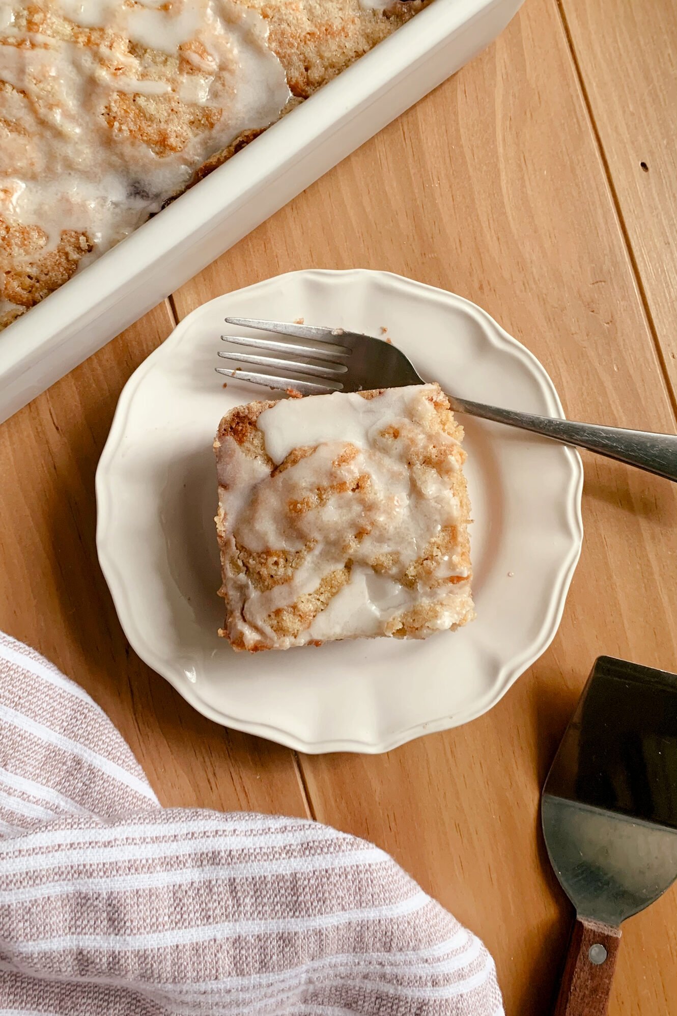 Fresh Milled Cherry Coffee Cake on a plate with a fork next to a tea towel and serving utensil on a wooden surface.