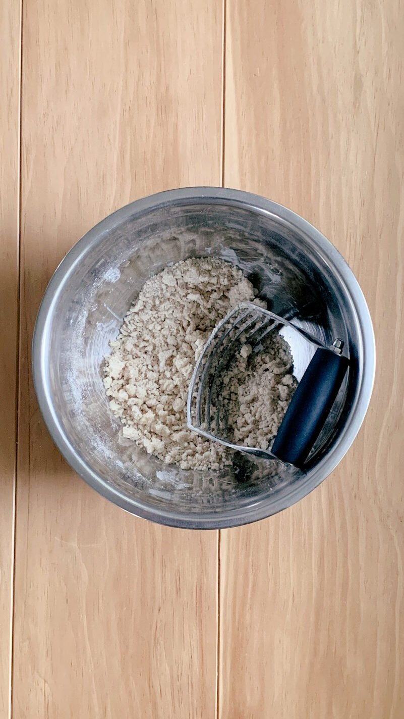 The completed streusel topping for fresh milled cherry coffee cake with a pastry blender, on a wooden surface