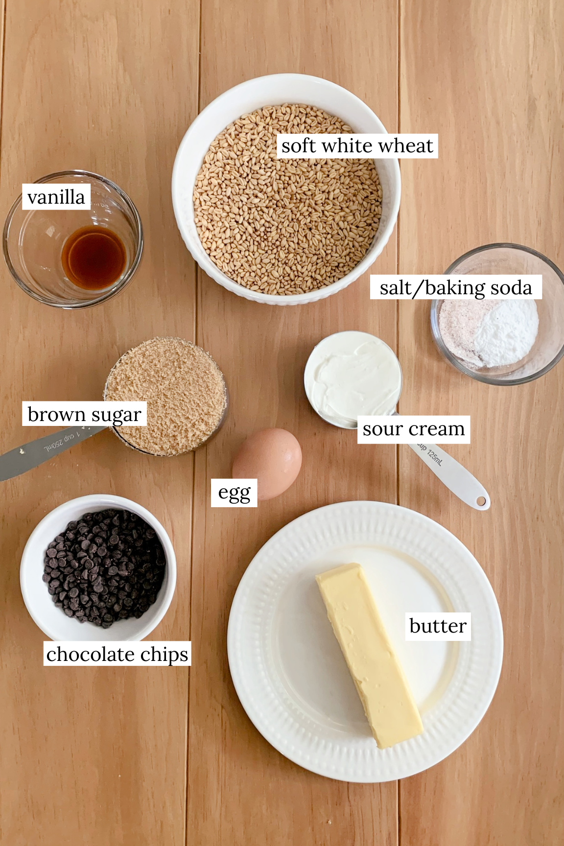 Ingredients for fresh milled chocolate chip cookies with sour cream laid out in bowls on a wooden surface