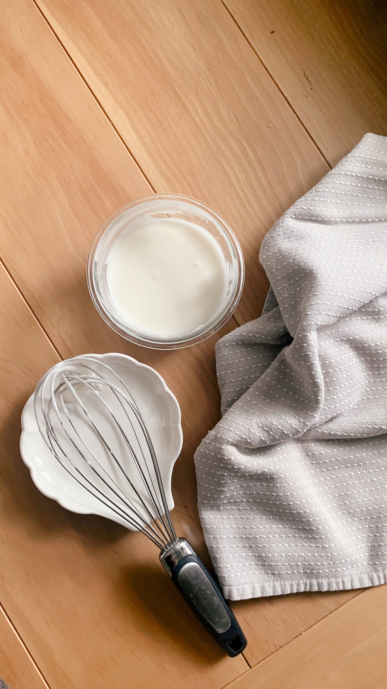 powdered sugar glaze in a glass bowl next to a tea towel and whisk on a wooden table