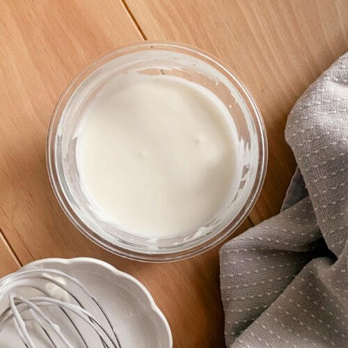powdered sugar glaze in a bowl next to a tea towel and a whisk on a wooden table