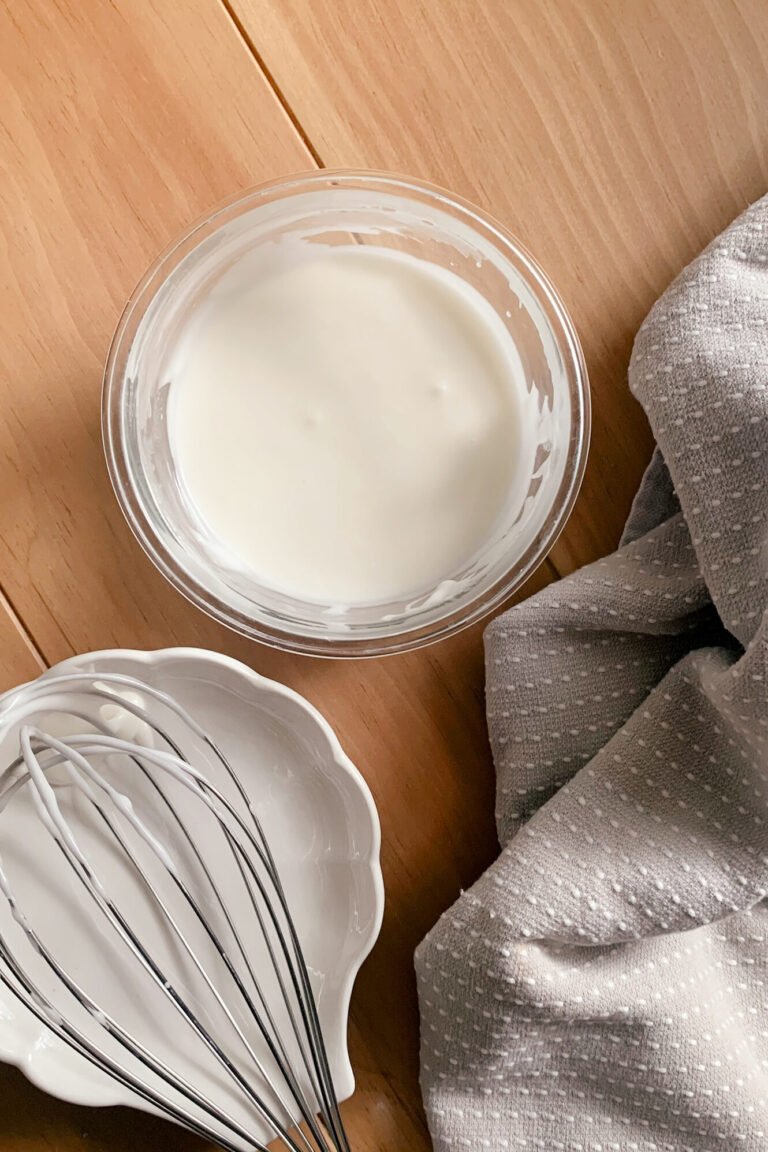 powdered sugar glaze in a bowl next to a tea towel and a whisk on a wooden table