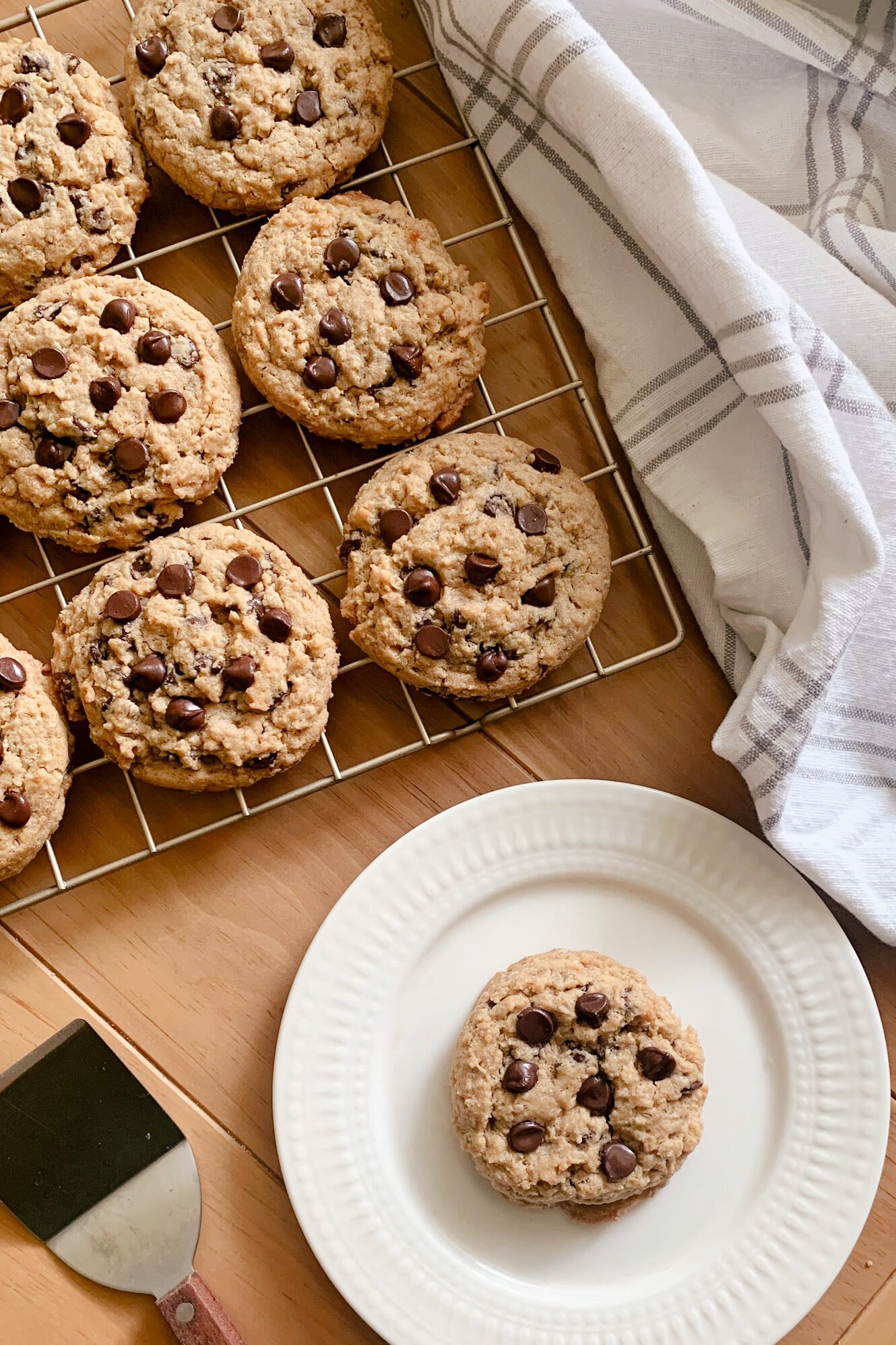 fresh milled peanut butter oatmeal chocolate chip cookies on a cooling rack next to a tea towel and a plate of a single cookie
