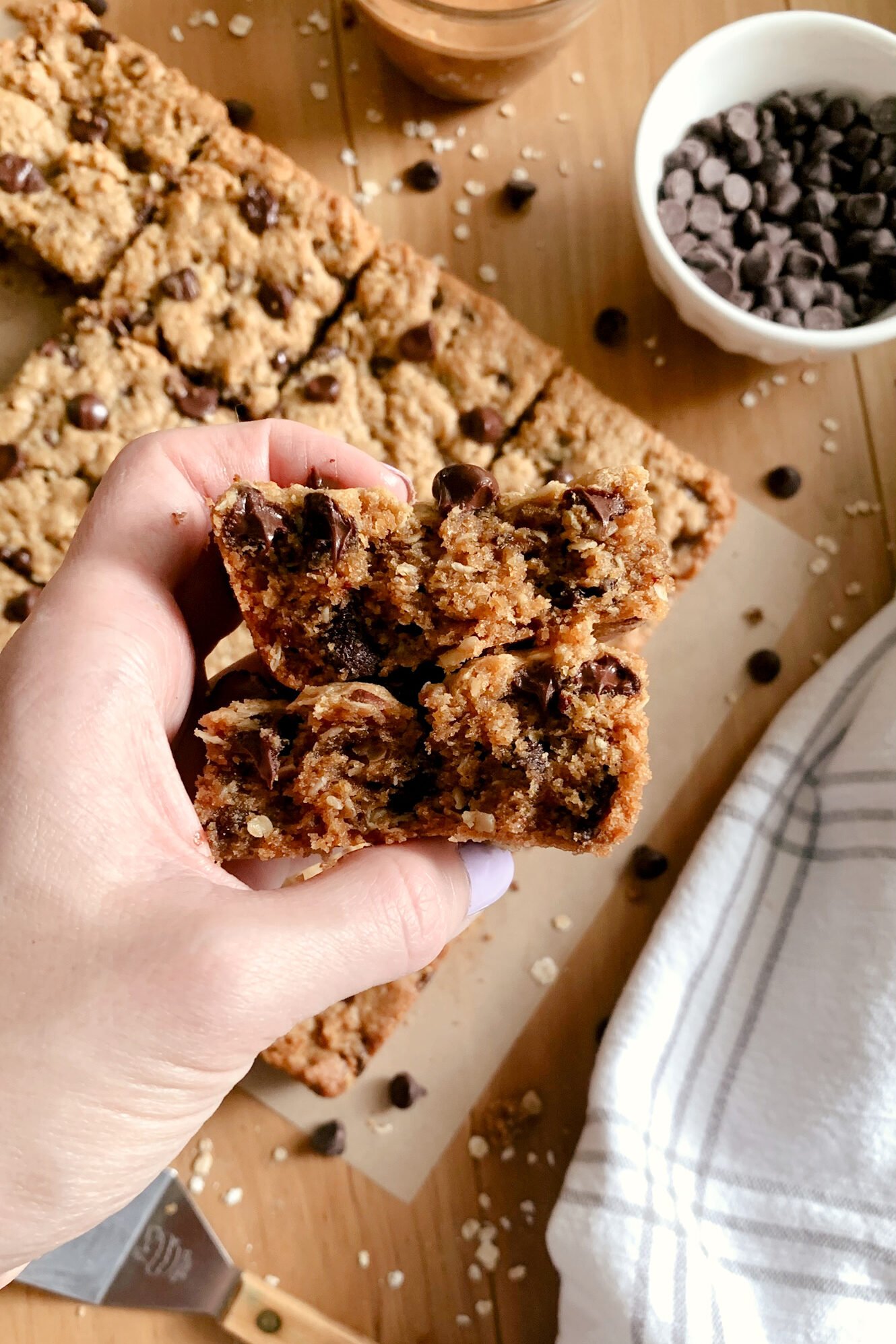 A hand holding two halves of the inside of a fresh milled peanut butter oatmeal chocolate chip cookie bar