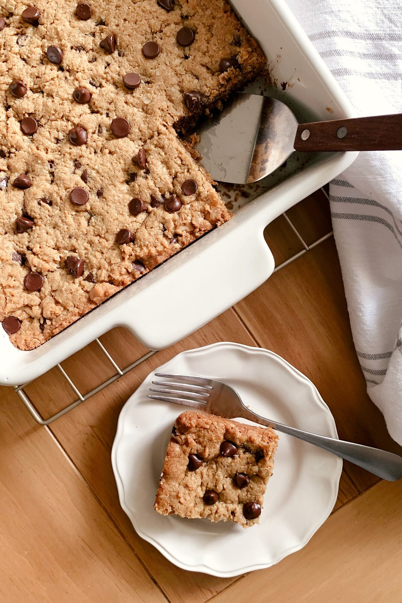 A fresh milled flour peanut butter oatmeal chocolate chip cookie bar on a plate with a fork next to the baking dish