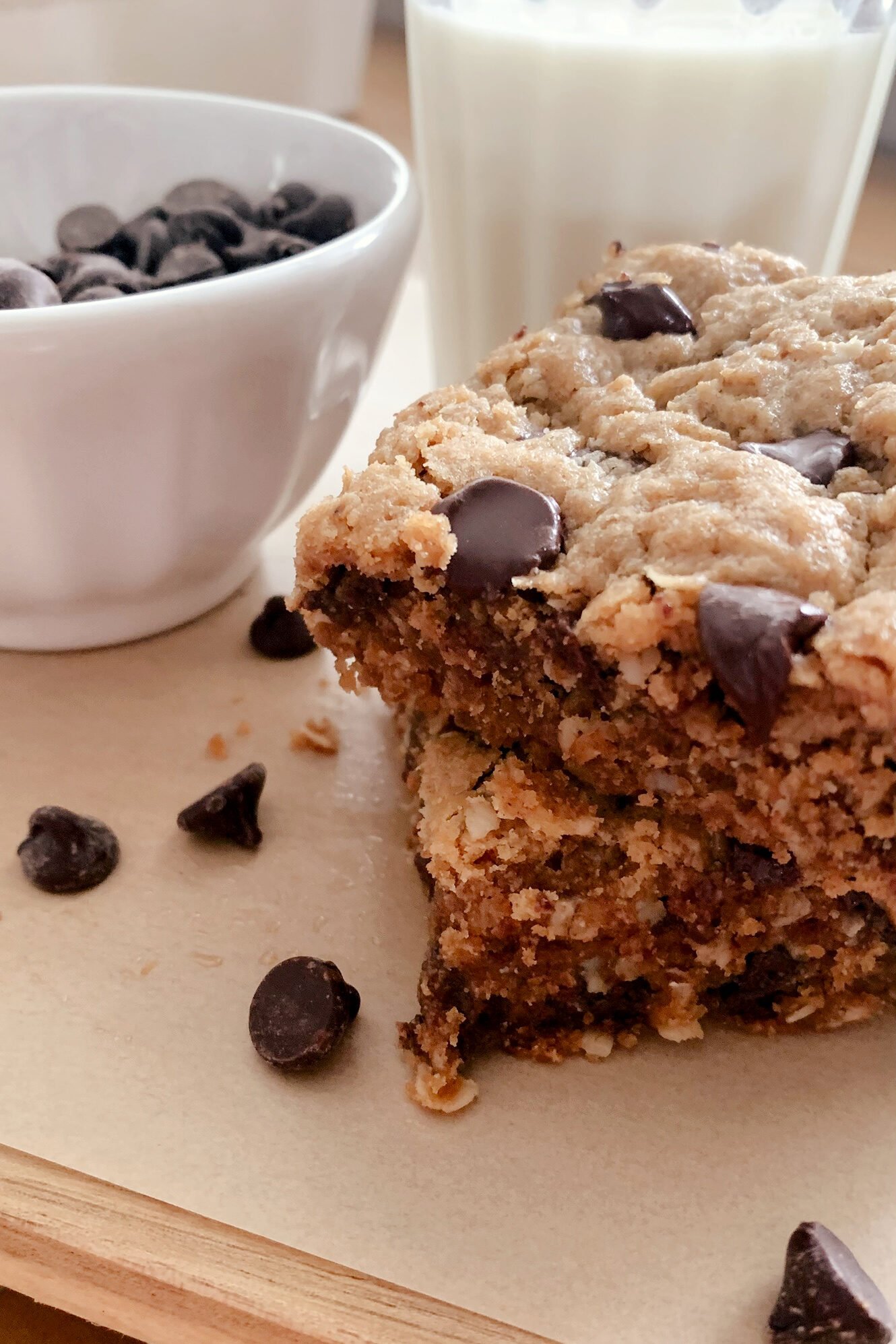 fresh milled peanut butter oatmeal chocolate chip cookie bars stacked next to a bowl of chocolate chips and a glass of milk